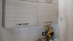 A room with a large wall-mounted cabinet, a small wooden side table with a vase, and a power outlet on the wall. - Petit Chateau - Room with kitchen (Montecatini Terme)