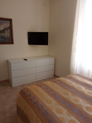 A bedroom with a bed, a TV mounted on the wall, a dresser, and a painting on the wall.