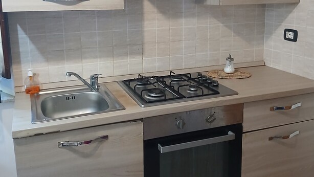 A kitchen with a gas stove, stainless steel sink, wooden cabinets, and a built-in oven. - Petit Chateau - Room with kitchen (Montecatini Terme)