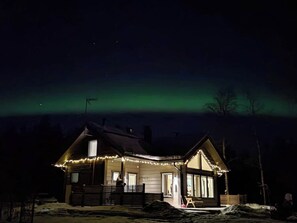 A house with a sloped roof, a porch with lights, and a view of the night sky.