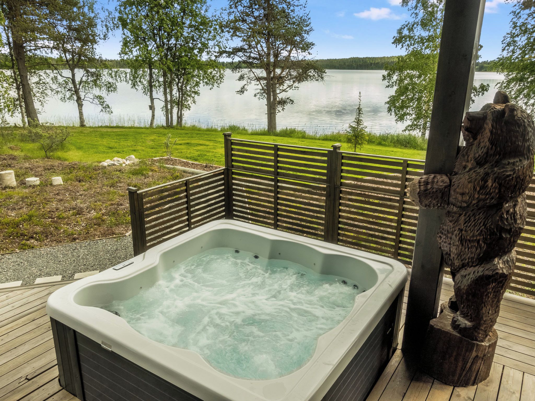 A hot tub on a wooden deck with a view of a lake and trees.