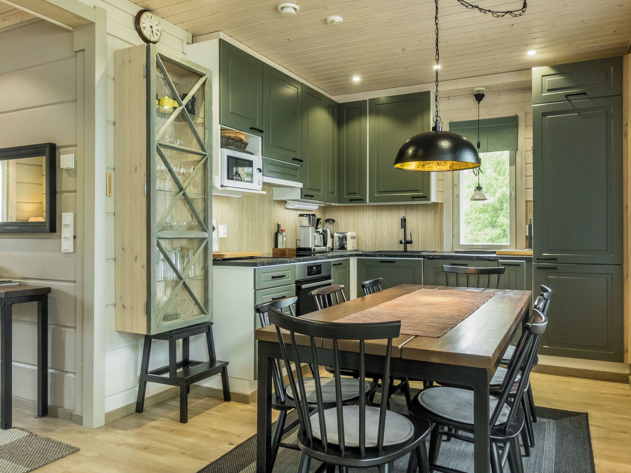 Una cocina moderna con armarios verde oscuro, una isla central con asientos y una lámpara colgante.