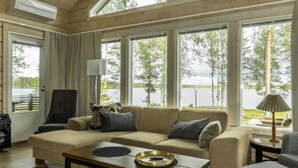A cozy living room with a sofa, armchairs, and a coffee table. Large windows offer views of a lake and trees.