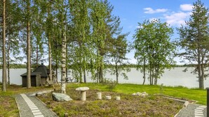 A lakeside garden with a wooden deck, a stone pathway, and a small wooden structure.