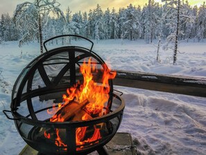 En eldstad av metall med flammor, placerad i en snötäckt miljö med träd.
