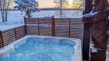 A hot tub with a wooden fence and a snow-covered tree in the background.