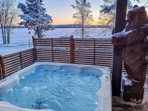 A hot tub with a wooden fence and a snow-covered tree in the background.