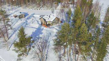 A snow-covered landscape with two houses surrounded by trees.
