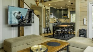 A modern living room with a flat-screen TV, a sofa, a coffee table, and a dining area with a wooden table and chairs.