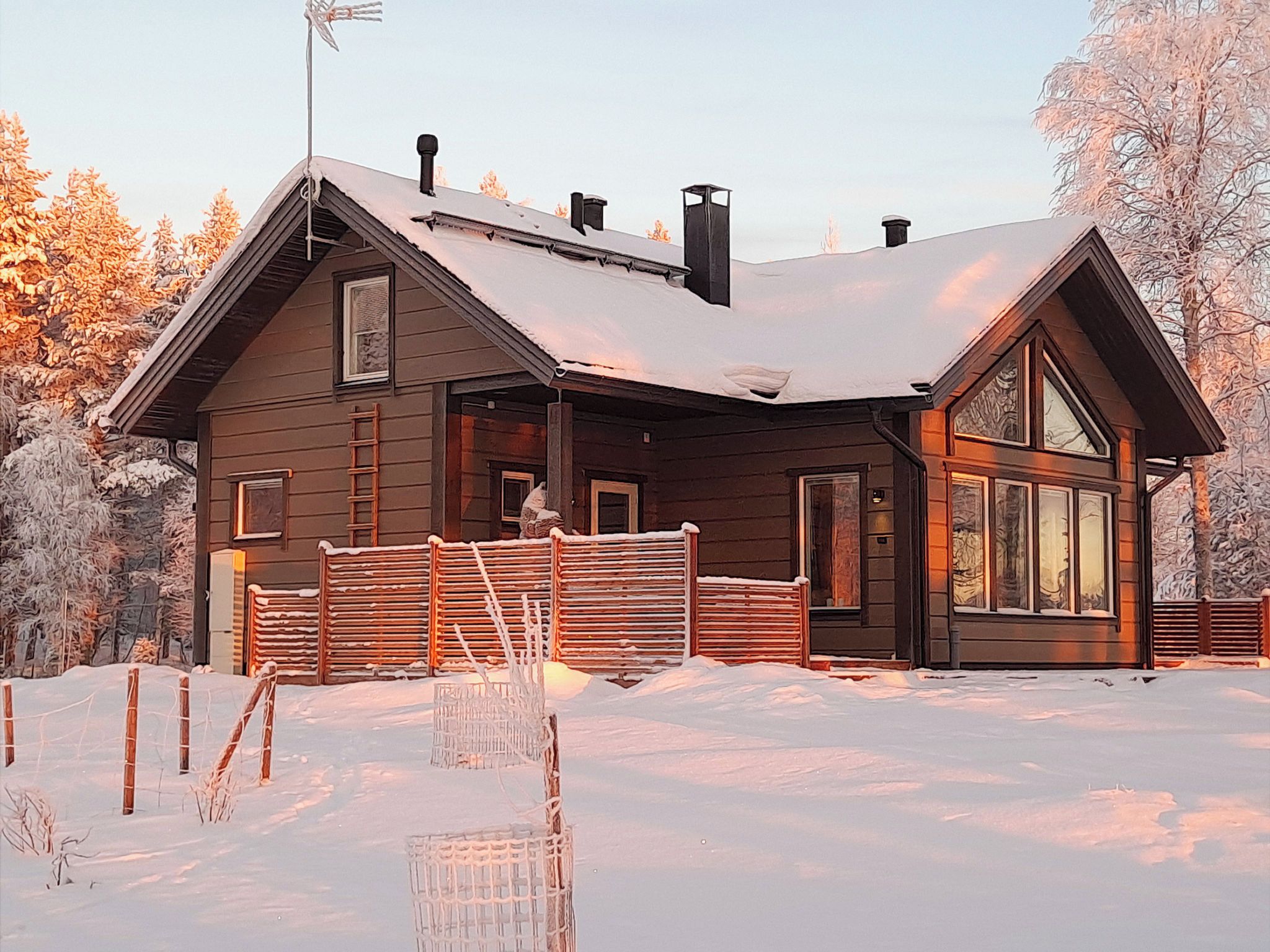A wooden cabin with a snow-covered roof, a chimney, and a large window.