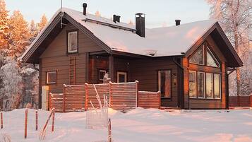 A wooden cabin with a snow-covered roof, a chimney, and a large window.