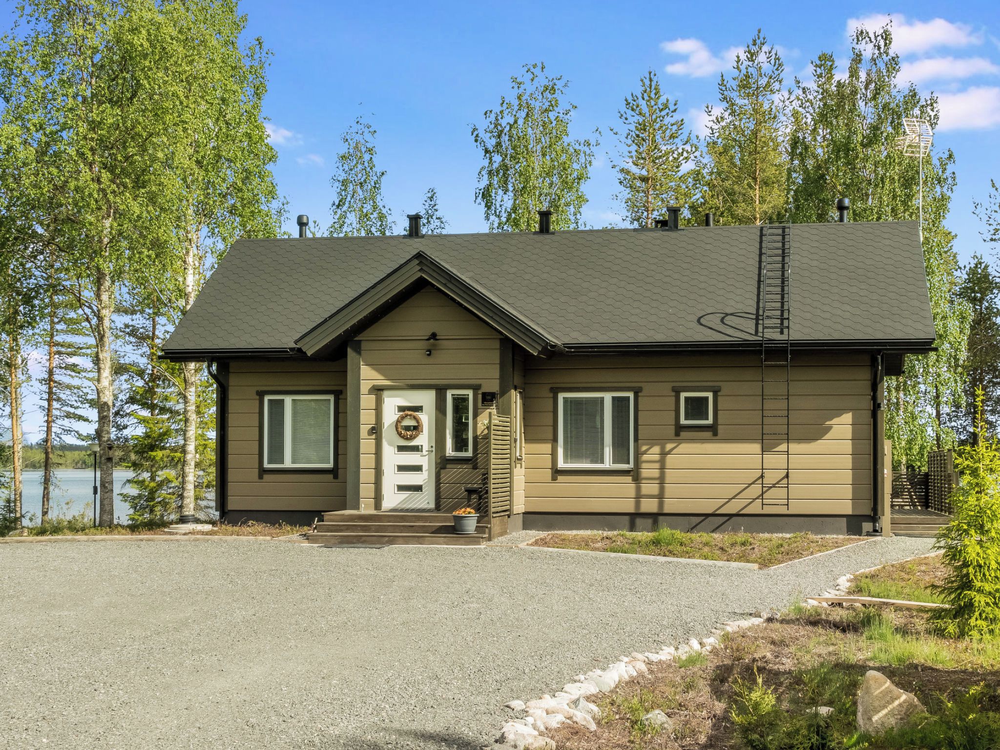 A two-story lodge with a front porch, a chimney, and a view of a lake.