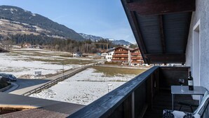 Uma varanda com mesa e cadeira, com vista para uma paisagem nevada com edifícios e montanhas.