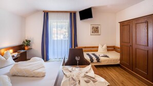 Quarto de hotel com cama, escrivaninha com luminária, cadeira, televisão fixada na parede e guarda-roupa.