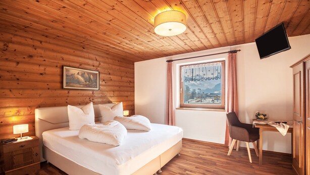 A wooden-paneled room with a bed, a desk, a chair, a TV, and a window with a view.