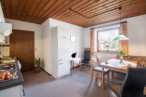 A compact kitchen with a microwave, sink, and potted plant. A dining area with a table, chairs, and a view of a building through a window.