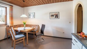 A dining area with a wooden table, chairs, a vase with flowers, and framed pictures on the wall.