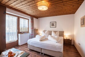 A bedroom with a wooden ceiling, a bed with white bedding, a bedside table, and a window with curtains.