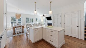 Un'ampia cucina con mobili bianchi, un tavolo da pranzo in legno e lampade a sospensione.