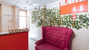 Un espace d’accueil avec un mur en briques rouges, une grande enseigne « DECHMARK », un fauteuil rouge moelleux et un mur décoré de feuilles vertes et de fleurs jaunes.