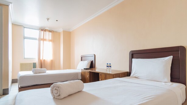 Une chambre d’hôtel avec deux lits, une table de chevet en bois et une fenêtre avec des rideaux.