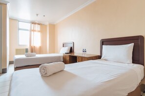 Una camera d'albergo con due letti, un comodino in legno e una finestra con tende.