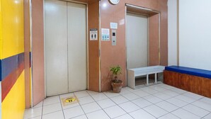 Un espace comprenant deux ascenseurs, une horloge, un panneau indiquant qu’il faut faire attention aux jeux d’ombre sur le visage, et un banc.