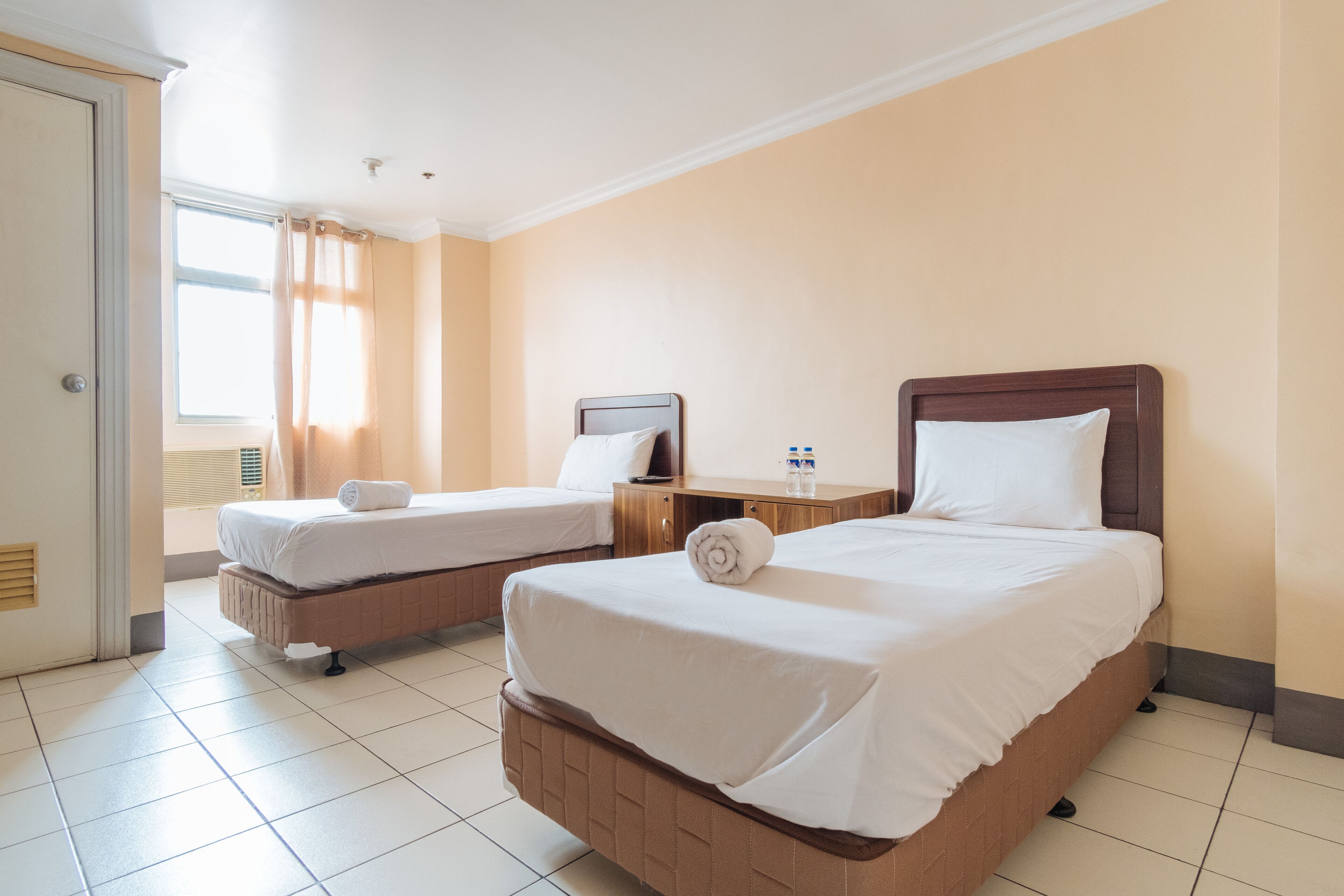 A hotel room with two beds, a desk, and a window with curtains.