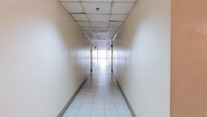 Un long couloir étroit aux murs et au sol recouverts de carreaux blancs, qui mène à une sortie lumineuse.