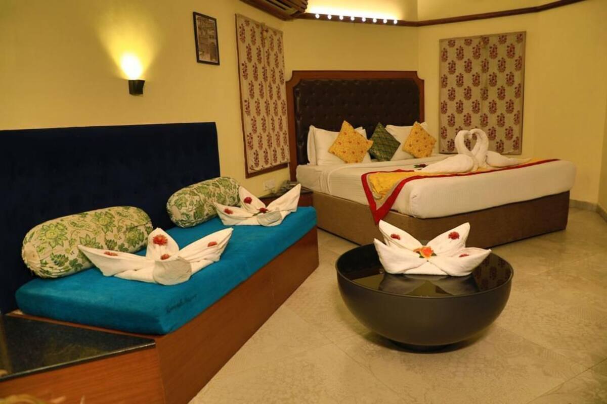 A hotel room with a blue sofa, a bed with floral-patterned bedding, and a black bowl with towels.
