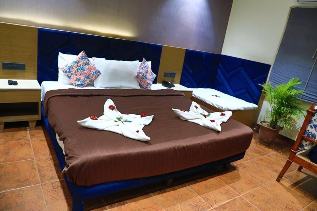 A hotel room with a large bed, a nightstand, a potted plant, and a wooden chair.