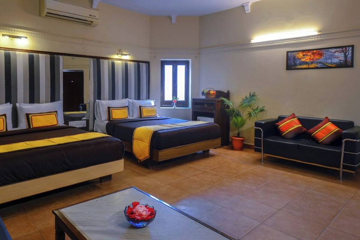 A hotel room with two beds, a sofa, a coffee table, and potted plants.