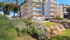 Un immeuble résidentiel à plusieurs étages, doté de balcons, entouré de jardins et de parterres de fleurs bien entretenus.