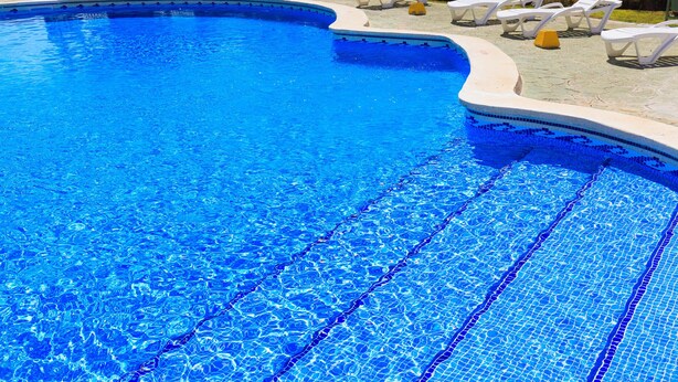 Une piscine à l’eau d’un bleu cristallin, entourée de chaises longues blanches et d’une terrasse carrelée.