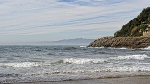 Une vue côtière avec des vagues, des falaises rocheuses et une chaîne de montagnes à l’horizon.