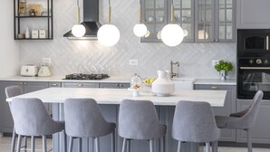 A modern kitchen with a central island, bar stools, pendant lighting, and a built-in oven. - Villa Velaga (Gruda)