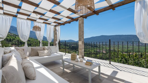 A terrace with a white sofa, a table, and a view of a mountainous landscape. - Villa Velaga (Gruda)