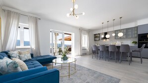 A modern living room with a blue sofa, a round coffee table, and a view of the kitchen and balcony. - Villa Velaga (Gruda)