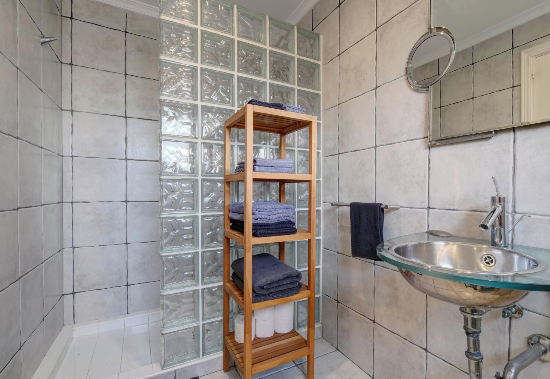 A bathroom with a glass shelf holding towels, a sink with a faucet, and a mirror.