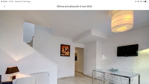 A modern living room with a sofa, a glass coffee table, a dining table with chairs, a TV mounted on the wall, and a staircase leading to another level. - Bright duplex (La Línea de la Concepción)