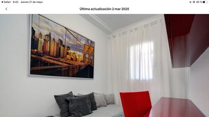 A modern hotel room with a cityscape painting, a bed with grey and red bedding, and a red accent chair. - Bright duplex (La Línea de la Concepción)