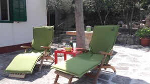 Two green lounge chairs with wooden frames and cushions, a small red table with a bottle and glasses, and a stone wall in the background. - Holiday Home Pavarotti (Supetar)