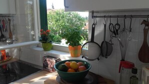 A kitchen with a window, potted plants, a bowl of fruit, and kitchen utensils hanging on the wall. - Holiday Home Pavarotti (Supetar)