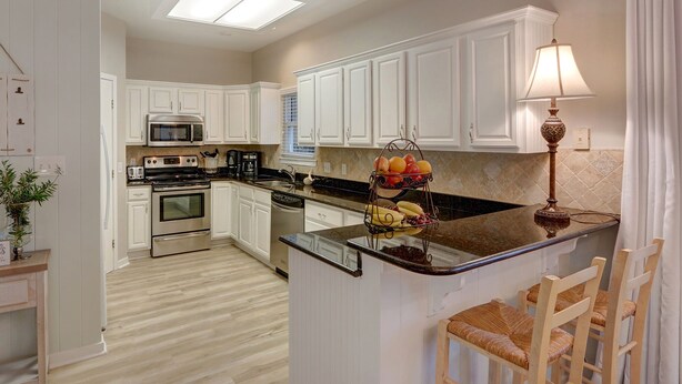 Una cocina moderna con armarios blancos, una isla central, microondas, horno y una cesta de frutas.