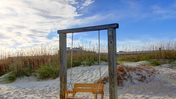A wooden swing set with a bench in a sandy area with sparse vegetation. - Spacious Home, Private Pool, Steps to the Beach (Tybee Island)