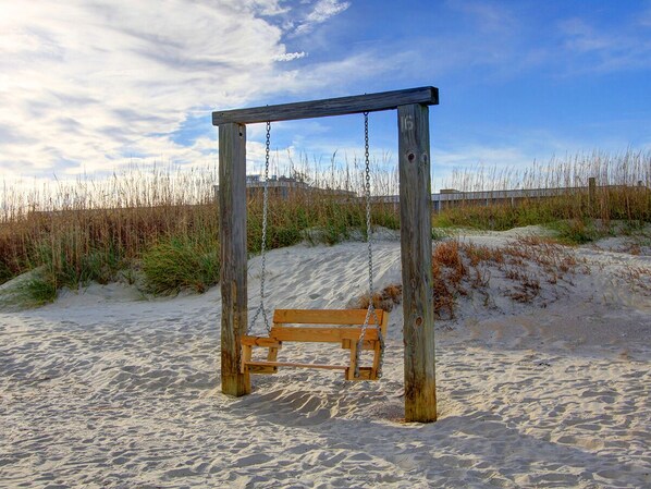 A wooden swing set with a bench in a sandy area with sparse vegetation. - Spacious Home, Private Pool, Steps to the Beach (Tybee Island)