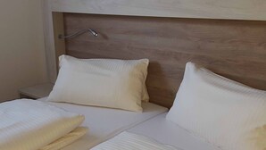 A neatly made bed with white linens and pillows, a wooden headboard, and a bedside table with a lamp.