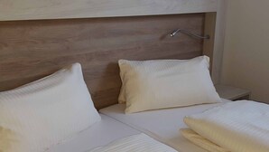A neatly made bed with white linens and pillows, a wooden headboard, and a bedside table with a lamp.