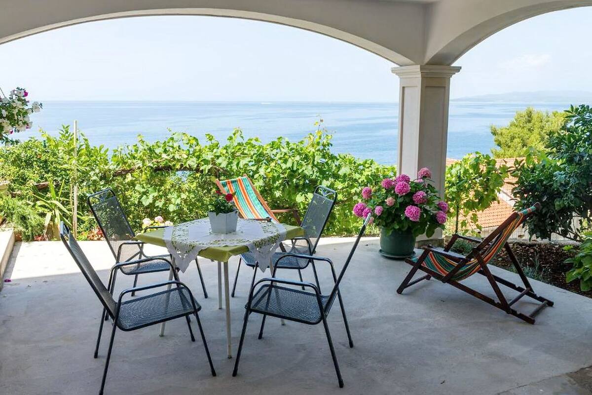 Un patio techado con una mesa, sillas, una hamaca y plantas en macetas.