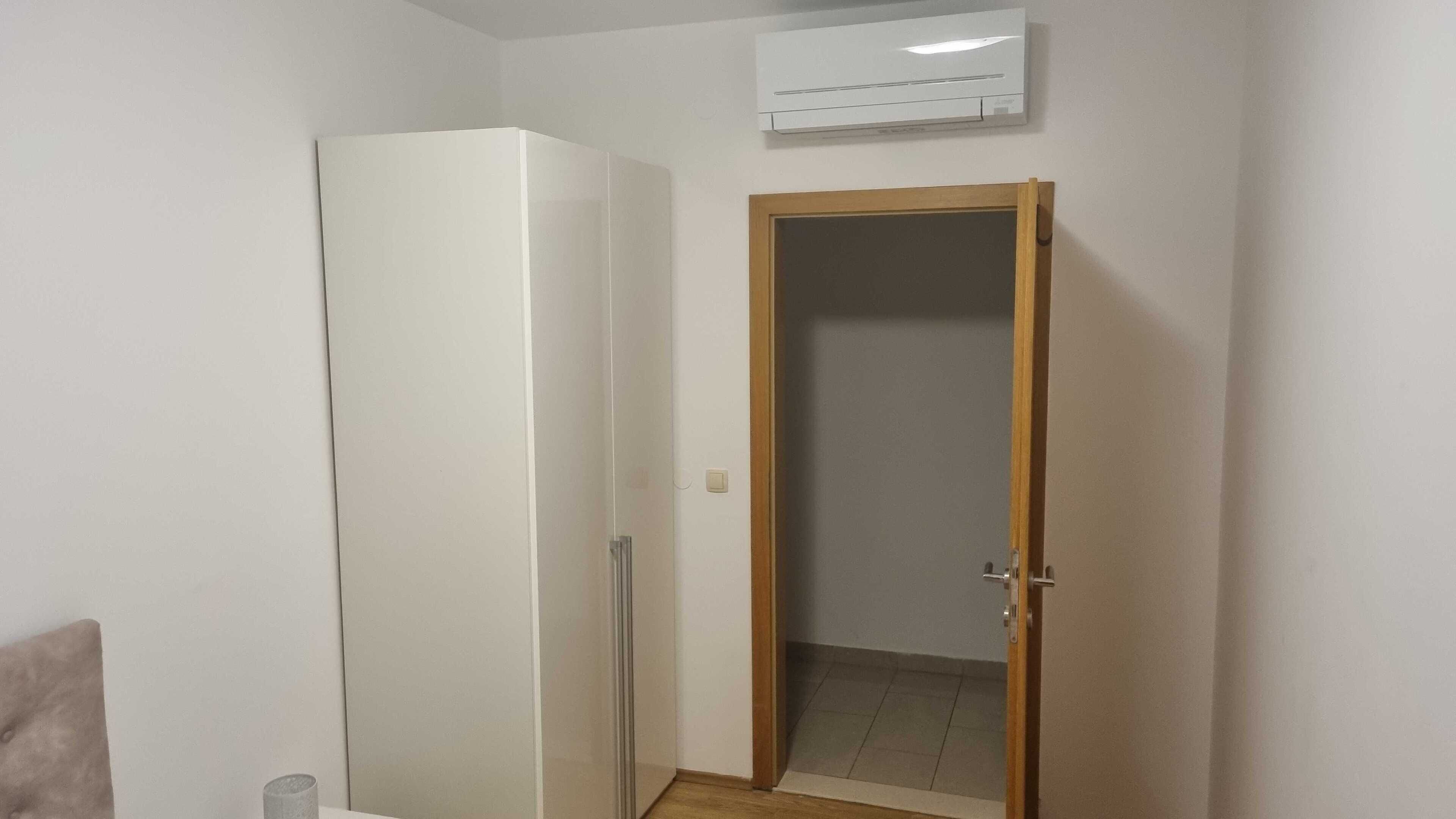 Una habitación con un refrigerador blanco, una puerta de madera y un equipo de aire acondicionado en la pared.